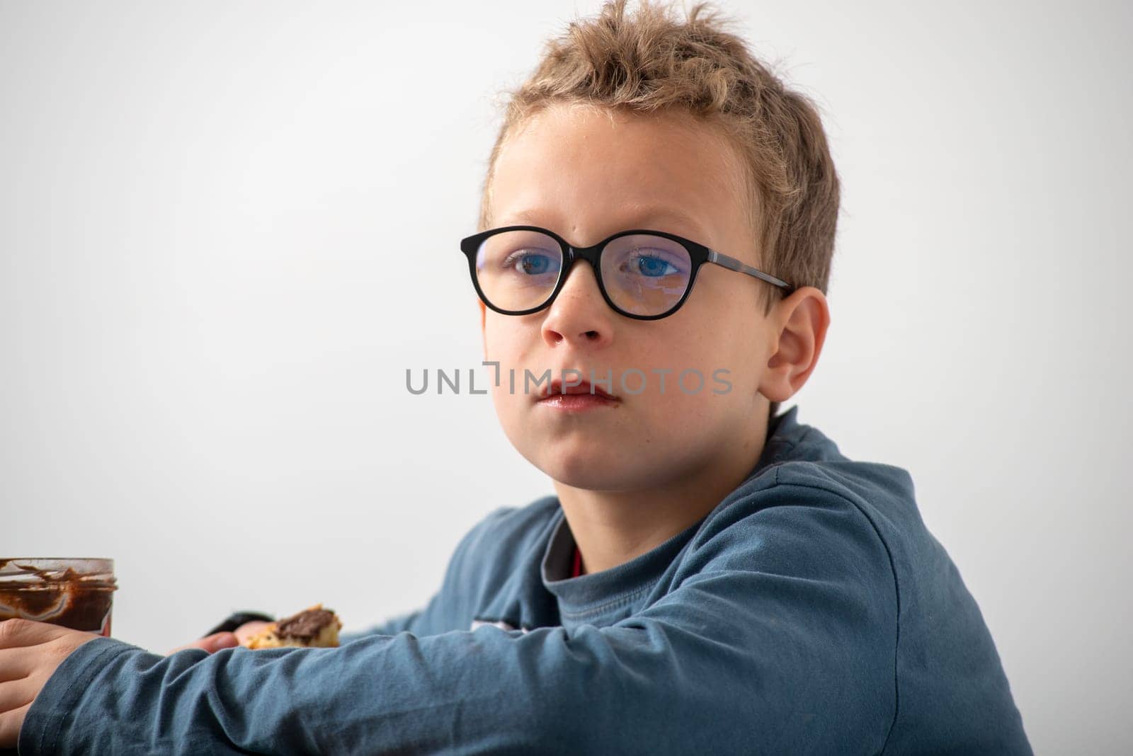 a pensive boy with eyeglasses eating a chocolate