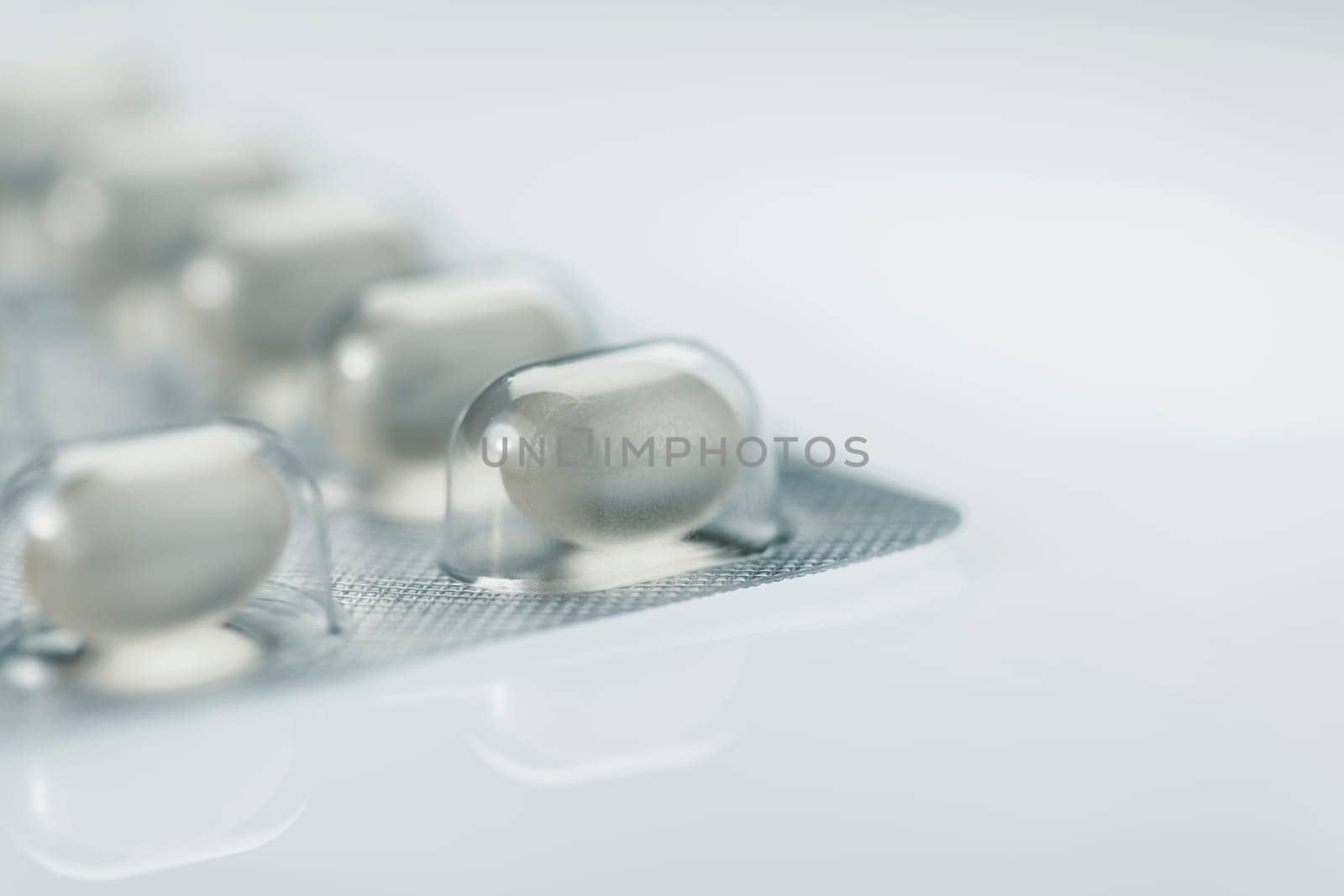 Macro shot of a foil packaging for tablet dragees isolated on white background with mirroring and focus on a single tablet in the foreground.
