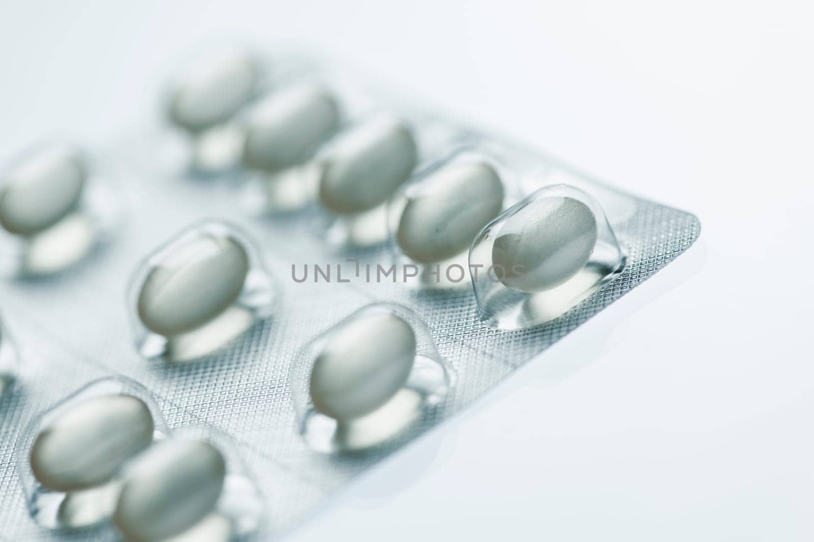 Sliced close-up of a foil packaging with oval tablets on white background with light shadows.