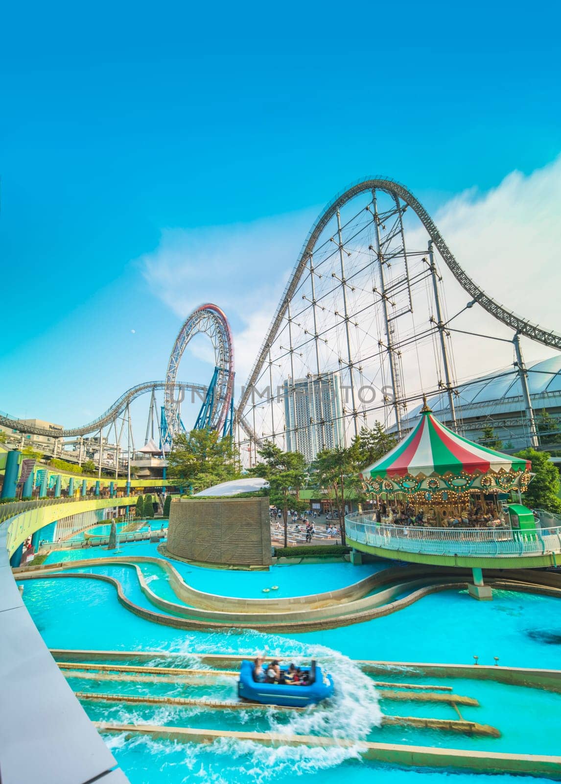 Laqua Tokyo Dome City Mall with its impressive roller coaster integrated in the gallery of its shopping center with a carousel  and water coaster under the summer blue sky.