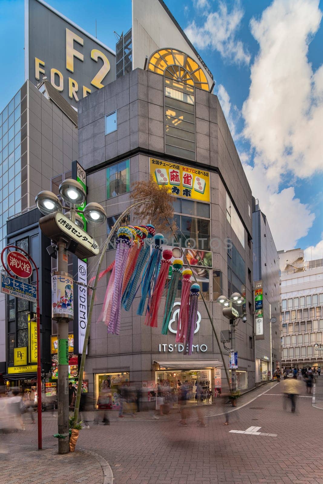 Summer blue sky on Shibuya Center Gai Street which literally means Shibuya Central District. The busiest street once intersected with Shibuya Station, it stretches for 350 meters and incorporates the adjacent streets of Bunkamura, Inokashira and Utagawa into its neighborhood. In 2011 the street was renamed Basketball Street in reference to the holy place of Japanese basketball which is the Yoyogi National Gymnasium to which this street leads. The photo is taken in summer at the Tanabata Star Festival where the portal is adorned with paper decorations in the shape of shooting stars for the occasion.