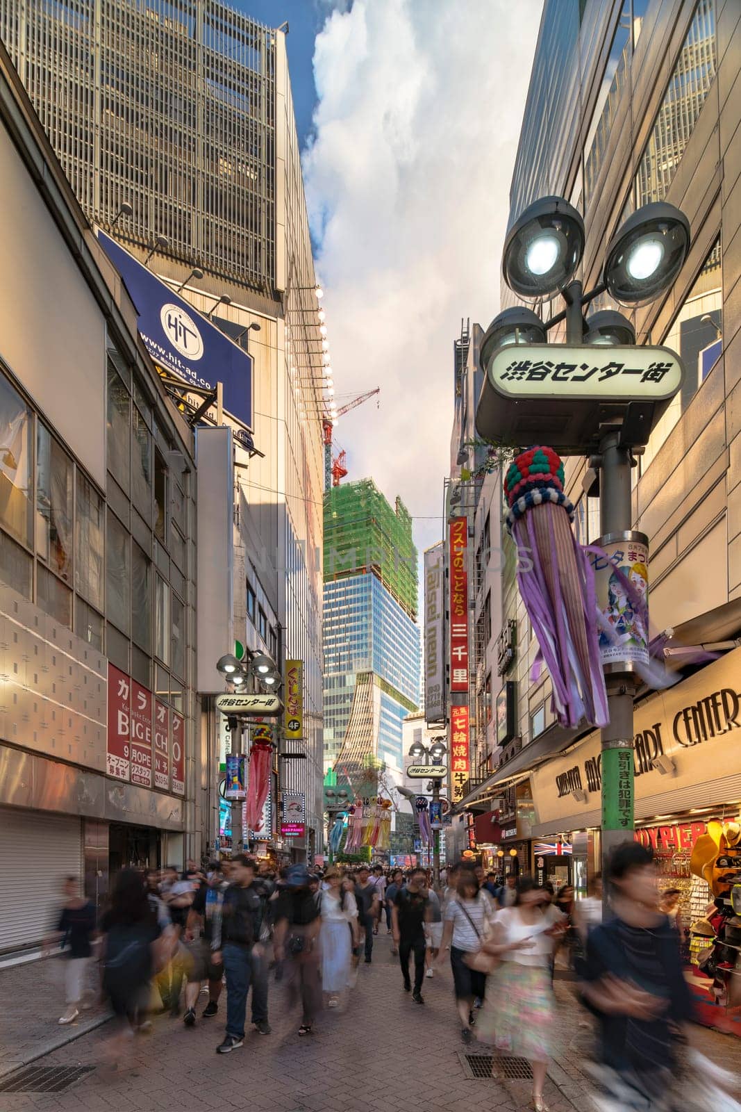 Summer blue sky on Shibuya Center Gai Street which literally means Shibuya Central District. The busiest street once intersected with Shibuya Station, it stretches for 350 meters and incorporates the adjacent streets of Bunkamura, Inokashira and Utagawa into its neighborhood. In 2011 the street was renamed Basketball Street in reference to the holy place of Japanese basketball which is the Yoyogi National Gymnasium to which this street leads. The photo is taken in summer at the Tanabata Star Festival where the portal is adorned with paper decorations in the shape of shooting stars for the occasion.
