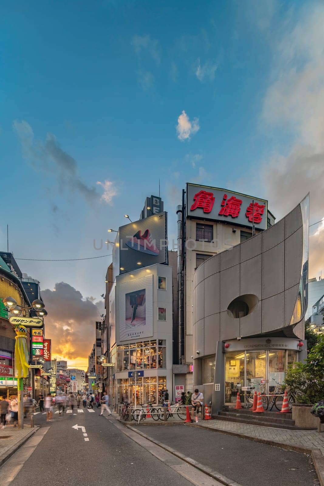 Sunset sky on owl iron mask Shaped of Shibuya Police Station Udagawa Kōban designed by architect Edward Suzuki and opened in April of 1985 in the Inokashira Steet of Shibuya Center Gai which literally means Shibuya Central District. The busiest street once intersected with Shibuya Station, it stretches for 350 meters and incorporates the adjacent streets of Bunkamura, Inokashira and Utagawa into its neighborhood. In 2011 the street was renamed Basketball Street in reference to the holy place of Japanese basketball which is the Yoyogi National Gymnasium to which this street leads. The photo is taken in summer at the Tanabata Star Festival where the portal is adorned with paper decorations in the shape of shooting stars for the occasion.