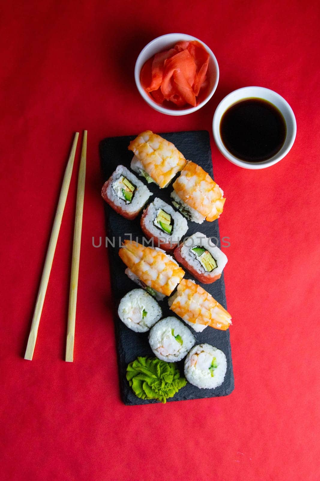 Sticks to reach for the roll, roll in the piece of packaging, next to the role of pickled ginger, everything stands on a red background. Top views