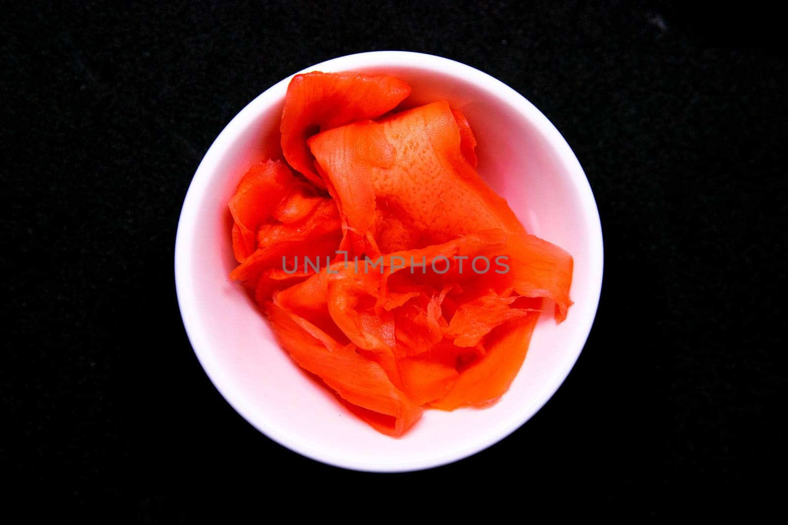 Sticks to reach for the roll, roll in the piece of packaging, next to the role of pickled ginger, everything stands on a red background. Top views