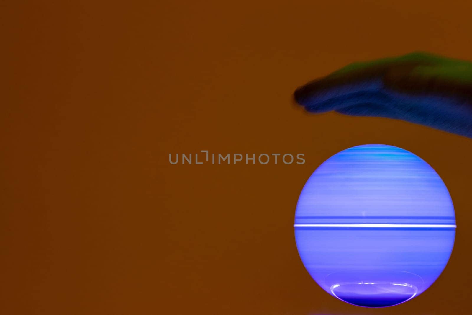 Mystery background. Closeup of glove over a mysterious bright blue glowing ball over red brown background. Macro shot with focus on the spinning globe.