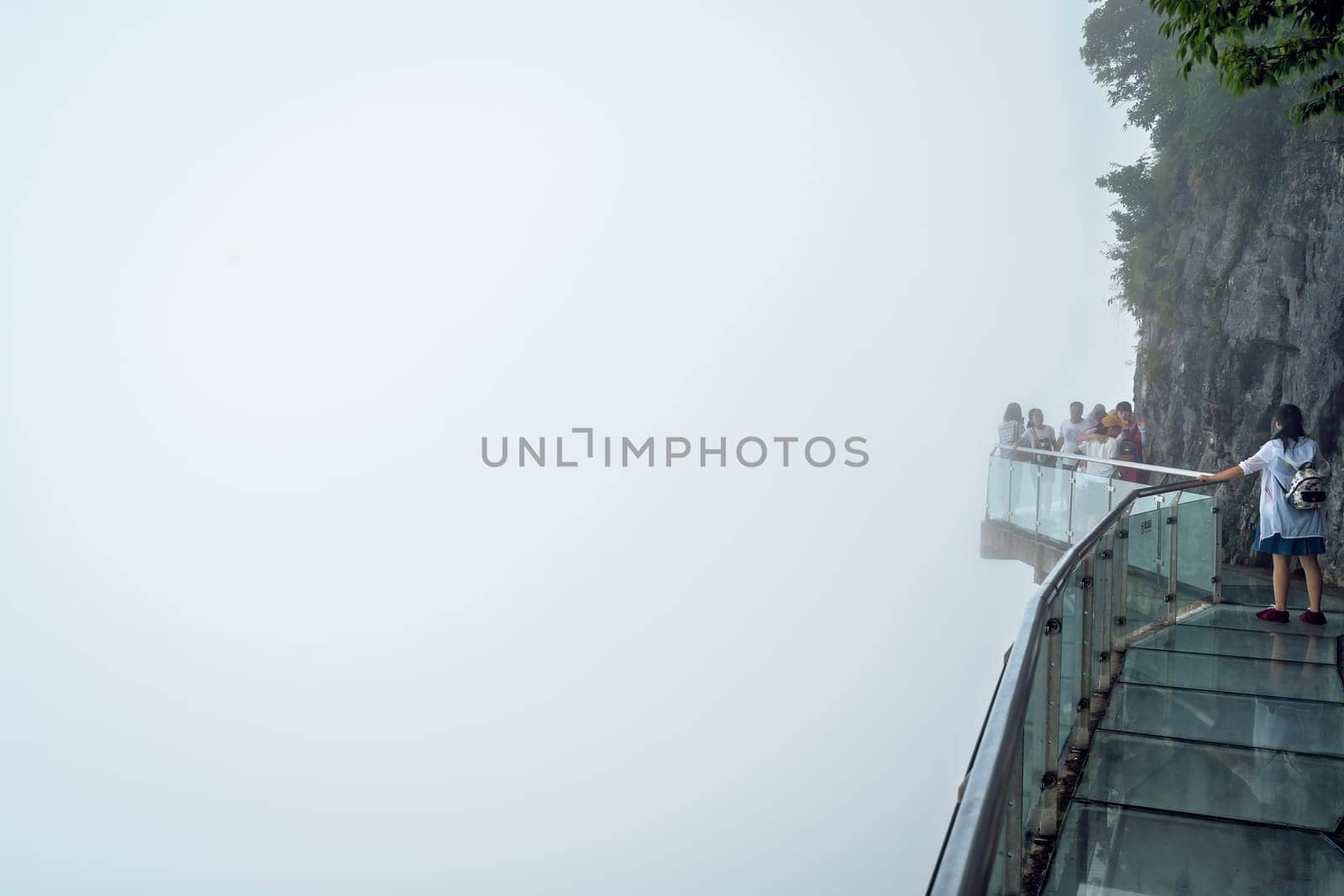 Zhangjiajie, China -  August 2019 : Tourists walking on a narrow glass pathway in Tianmenshan nature park