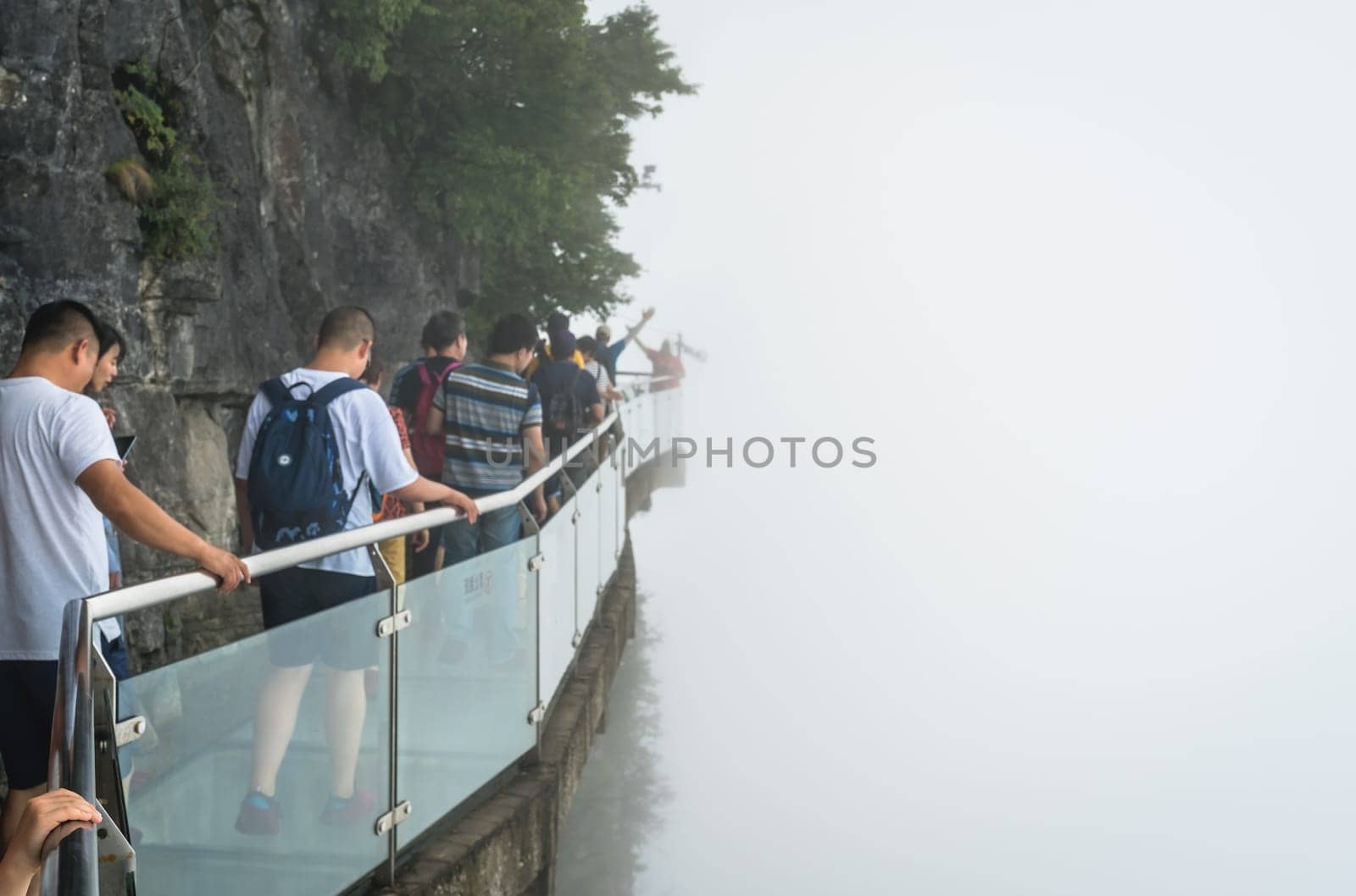 Zhangjiajie, China -  August 2019 : Tourists walking on a narrow glass pathway in Tianmenshan nature park