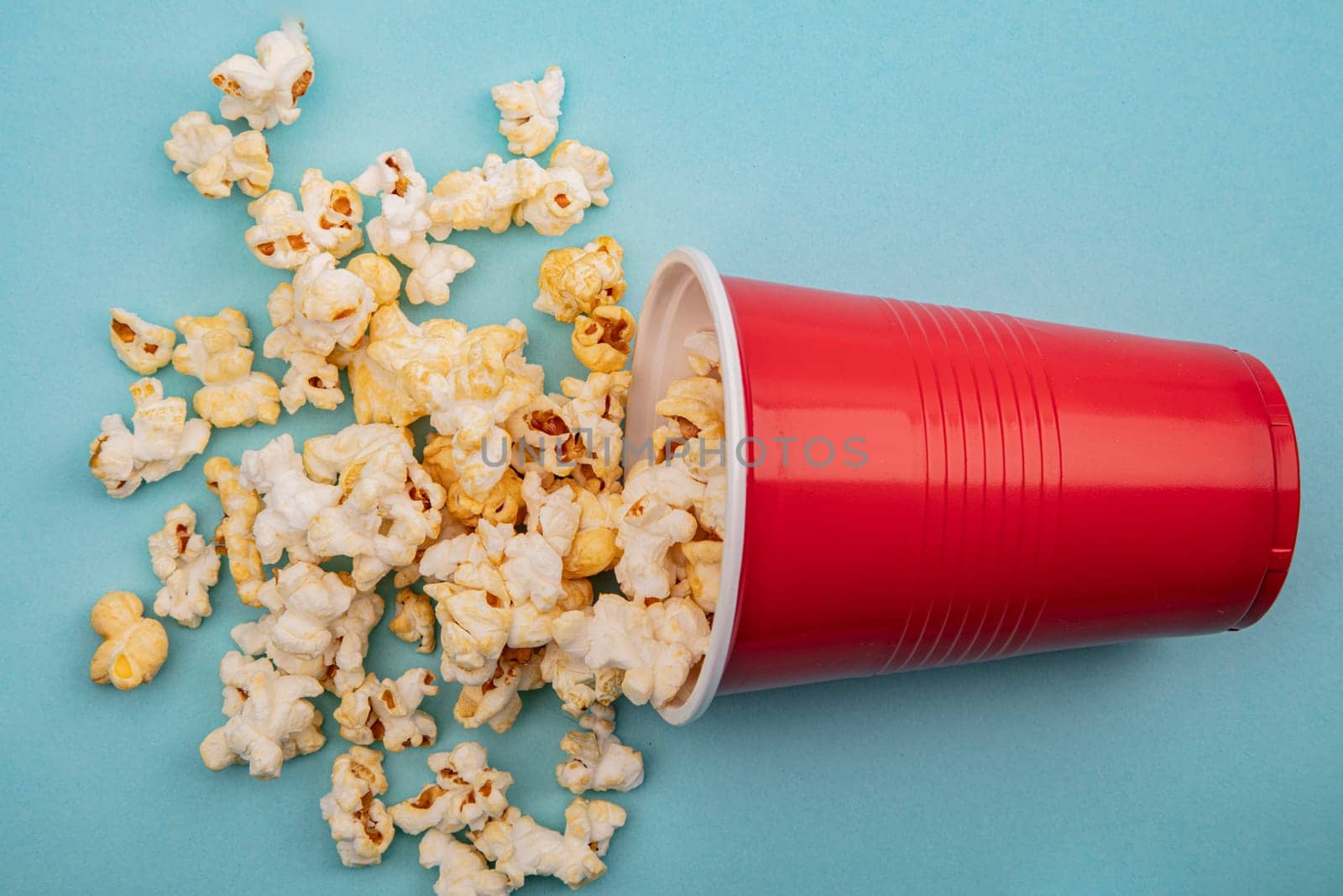 Crunchy Popcorn in plastic cup on bright blue background
