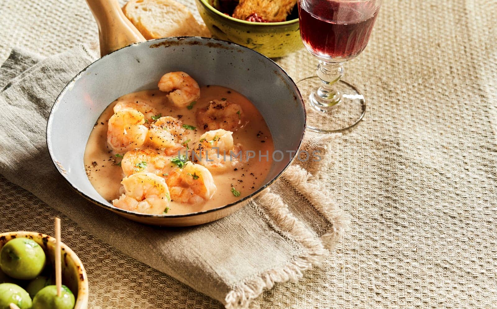 Scampi lobsters in cheese cream sauce served in old pan on rustic table with olives, bread and red wine. Traditional Spanish kitchen studio shot with copy space on linen tablecloth