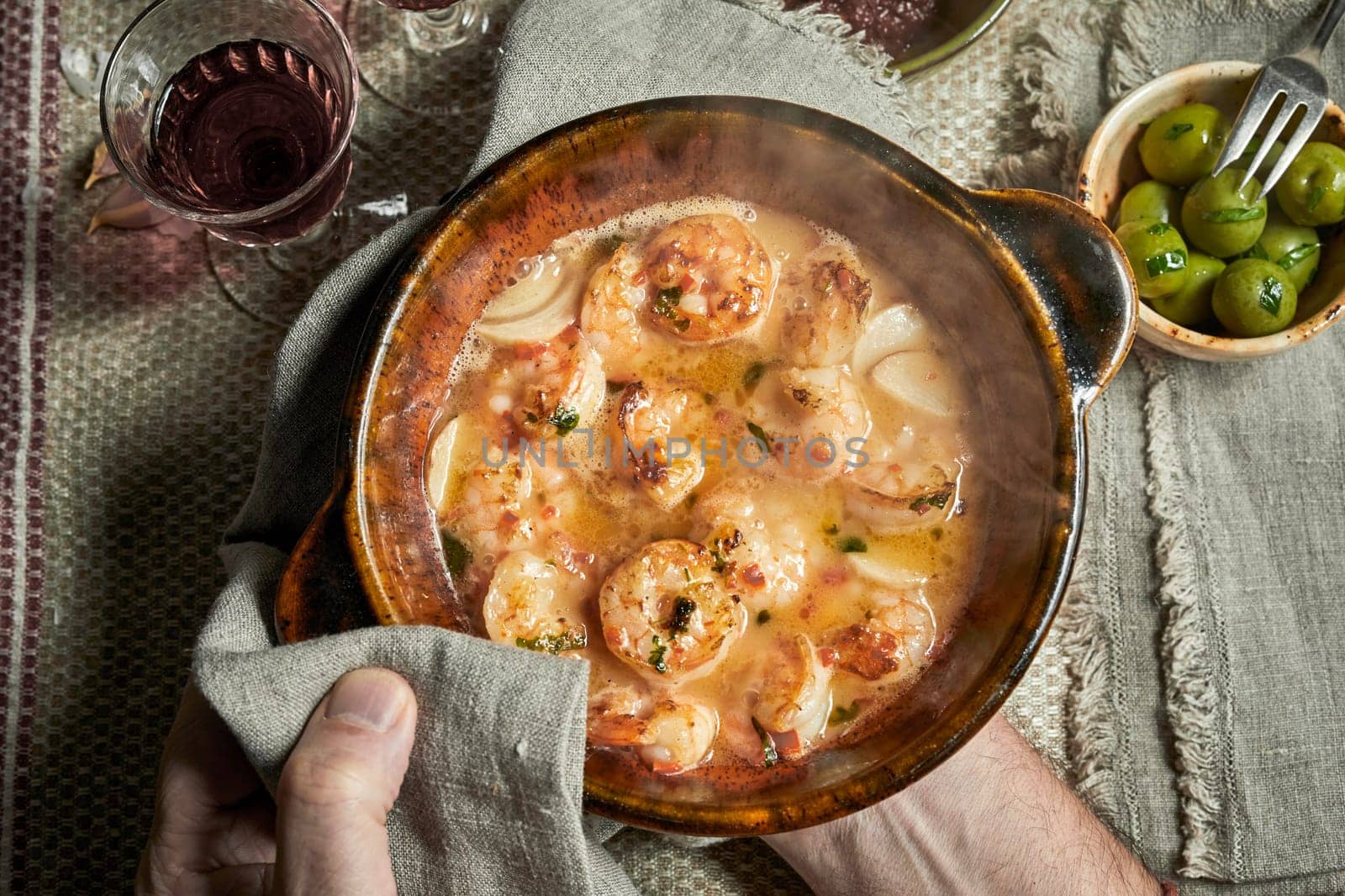 Chef serving a dish of scampi in savory sauce with fresh herbs and spices in an overhead view of his hands over a rustic table