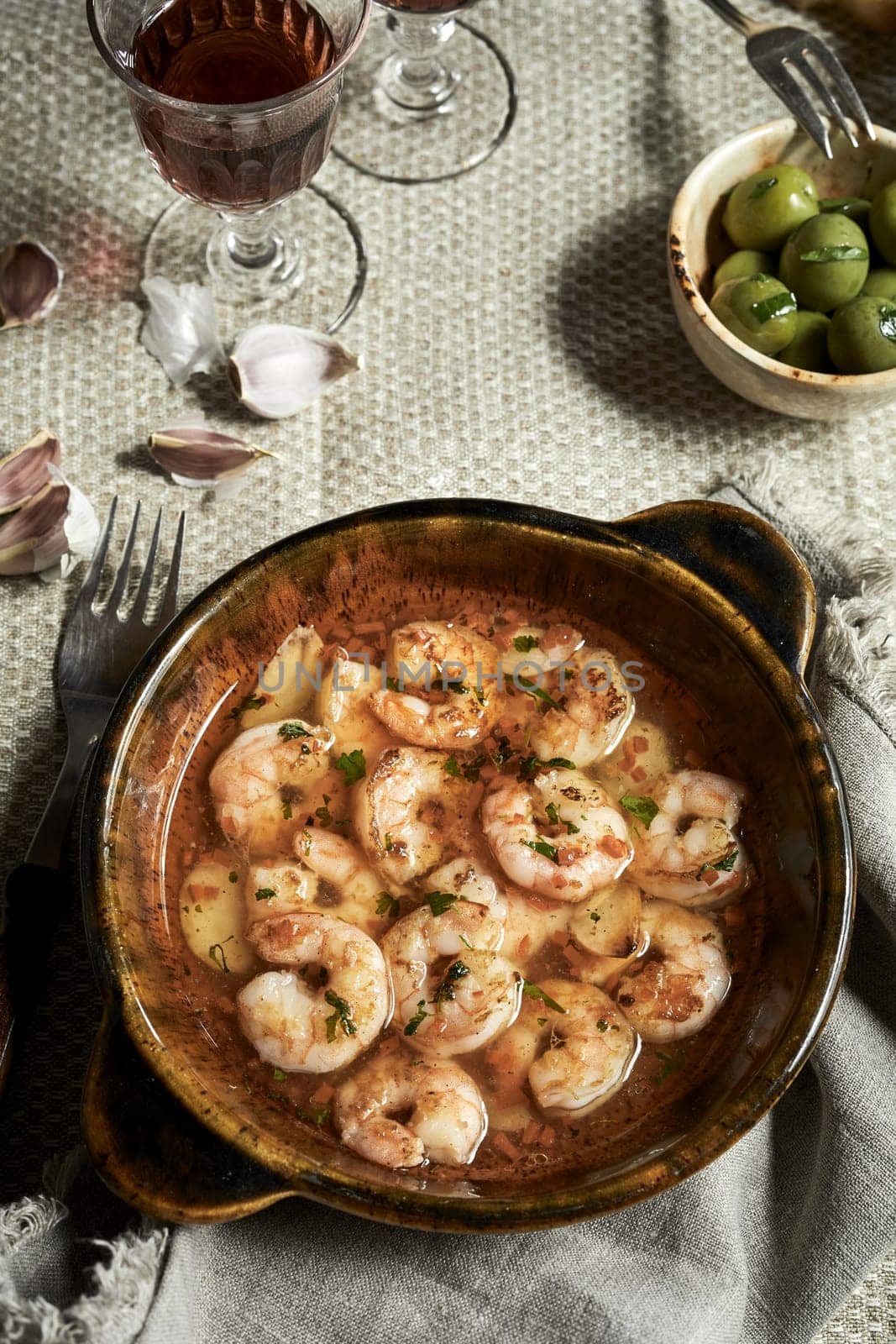 Hot spicy Spanish Gambas piri-piri or scampi peri peri served on a rustic table in a pan with glass of red wine in a top down view
