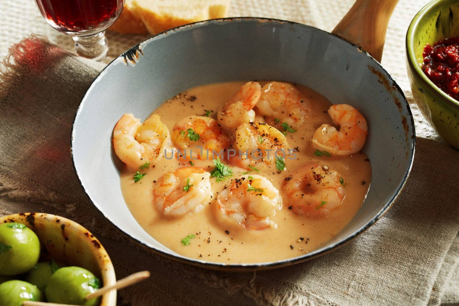Close-up on scampi lobsters in cheese-cream sauce served in old small pan with olives and glass of wine in a rustic style restaurant