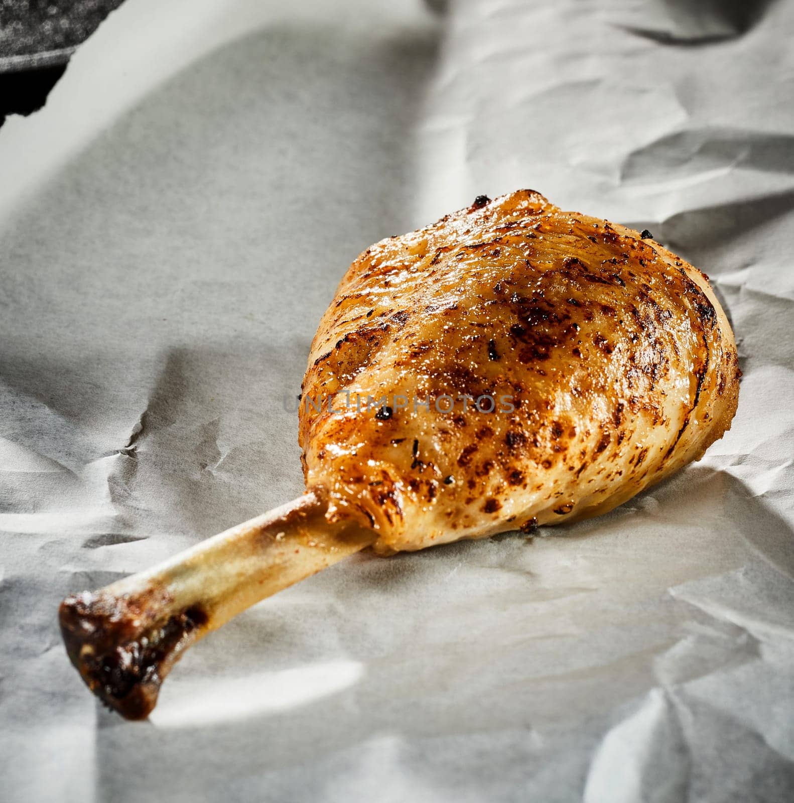 Grilled seasoned spicy chicken leg or drumstick on crumpled white paper in close up for menu advertising