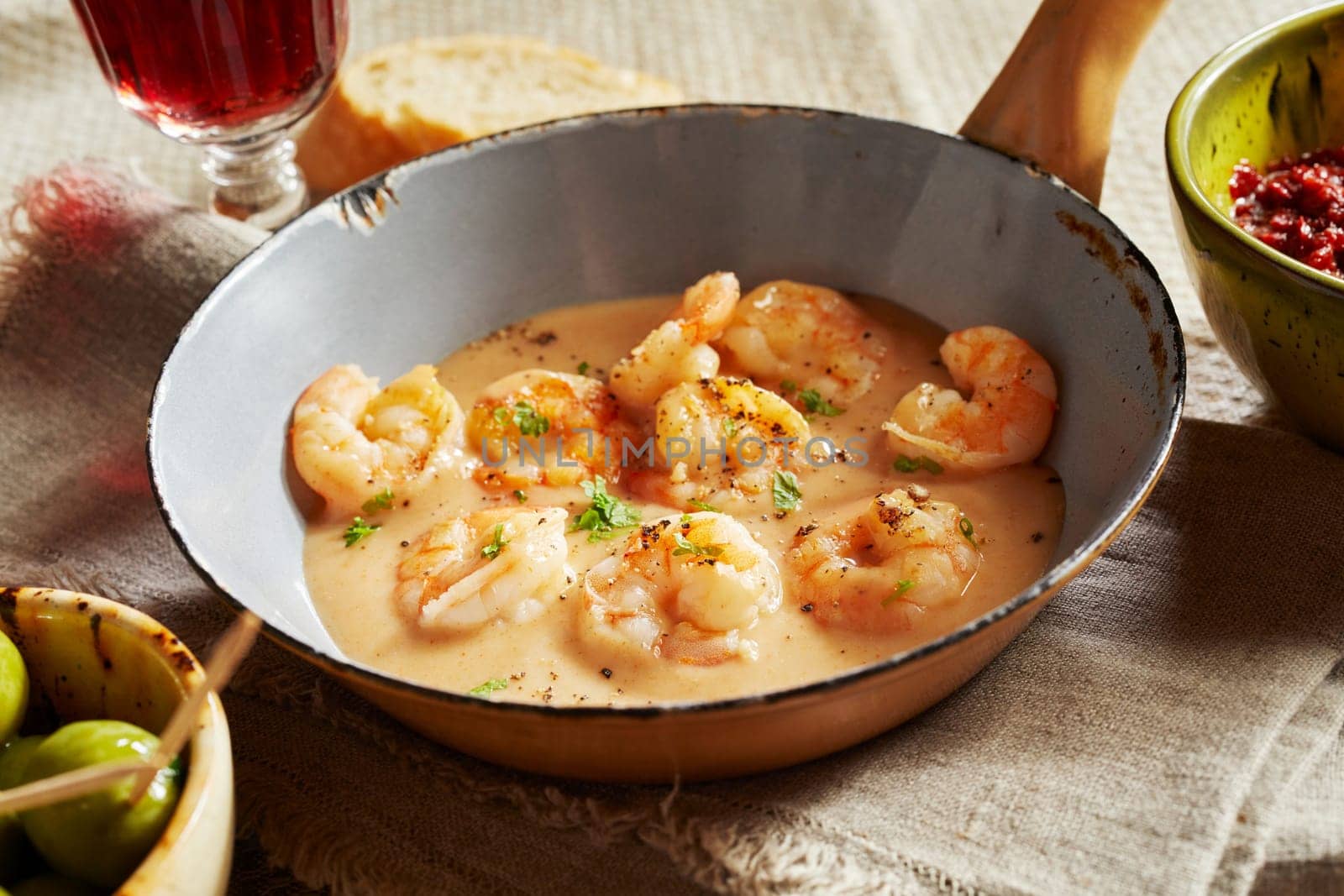Scampi lobsters in cheese-cream sauce or kase sahne sauce served in an old small pan on linen towel in a restaurant with rustic style or country house, with bowl of green olives and red wine