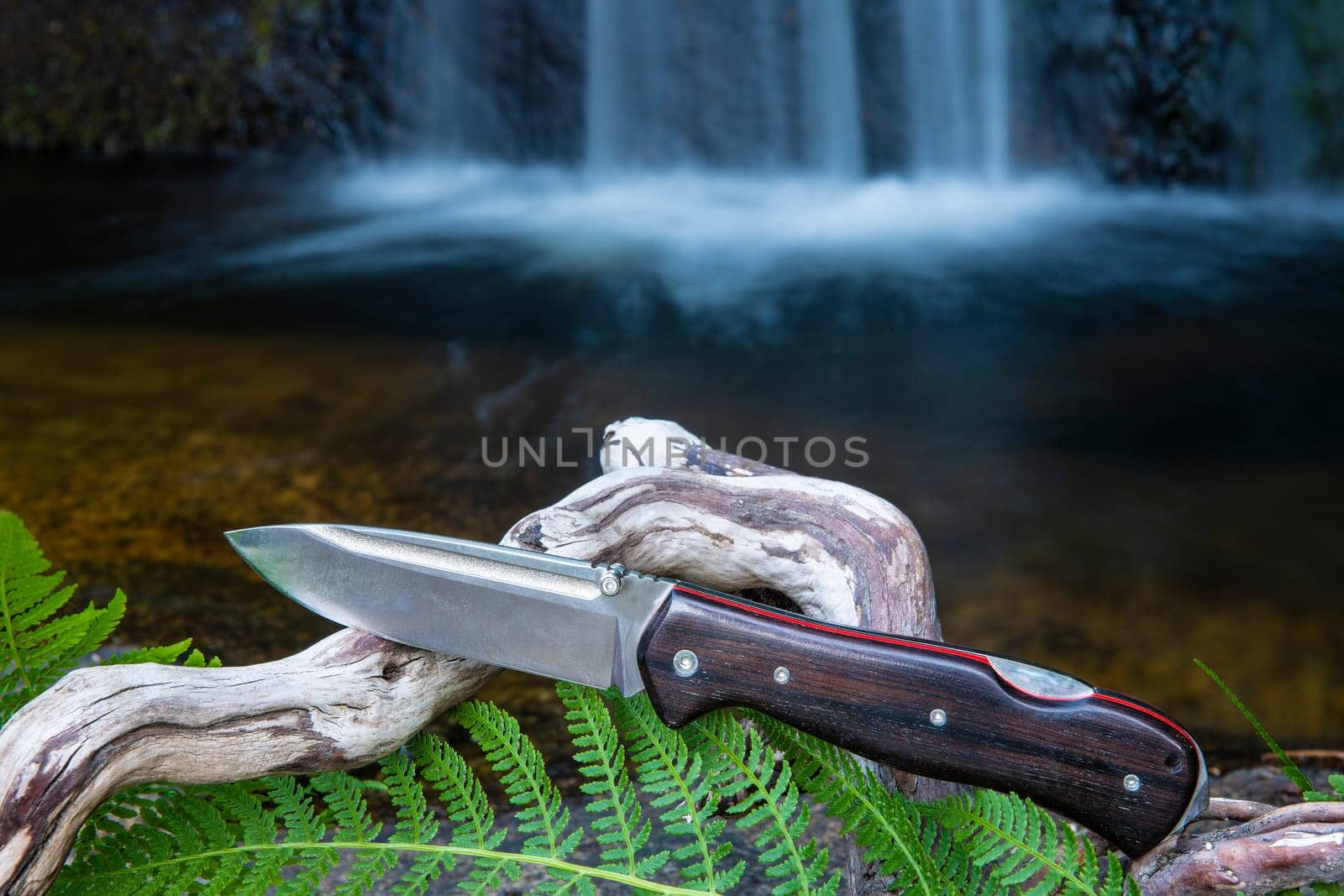 knife for bushcraft and survival in the wild near to a waterfall