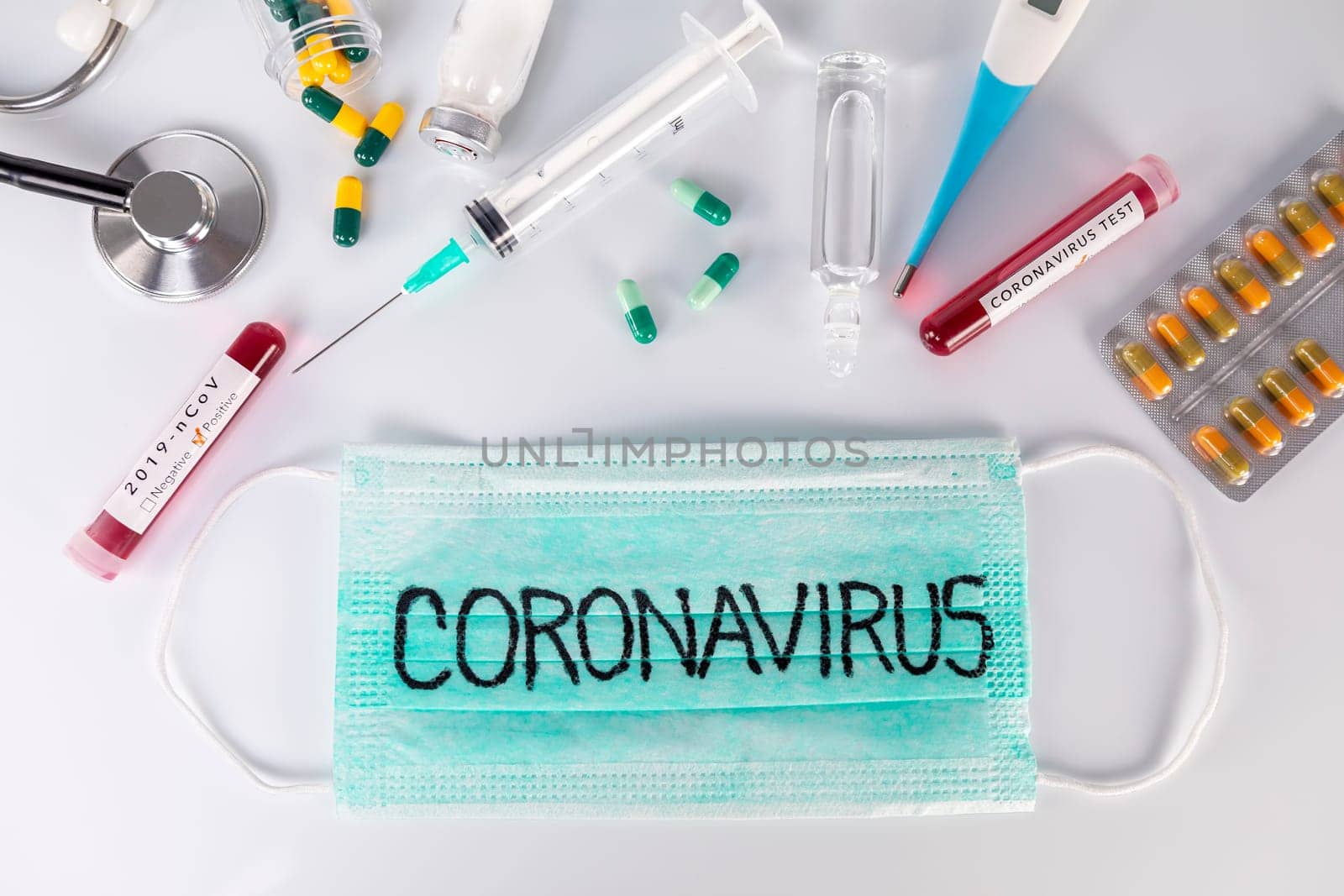 Protective medical mask with Coronavirus text and medical ampoules stethoscope thermometer and pills. Virus test and research for treatment concept.