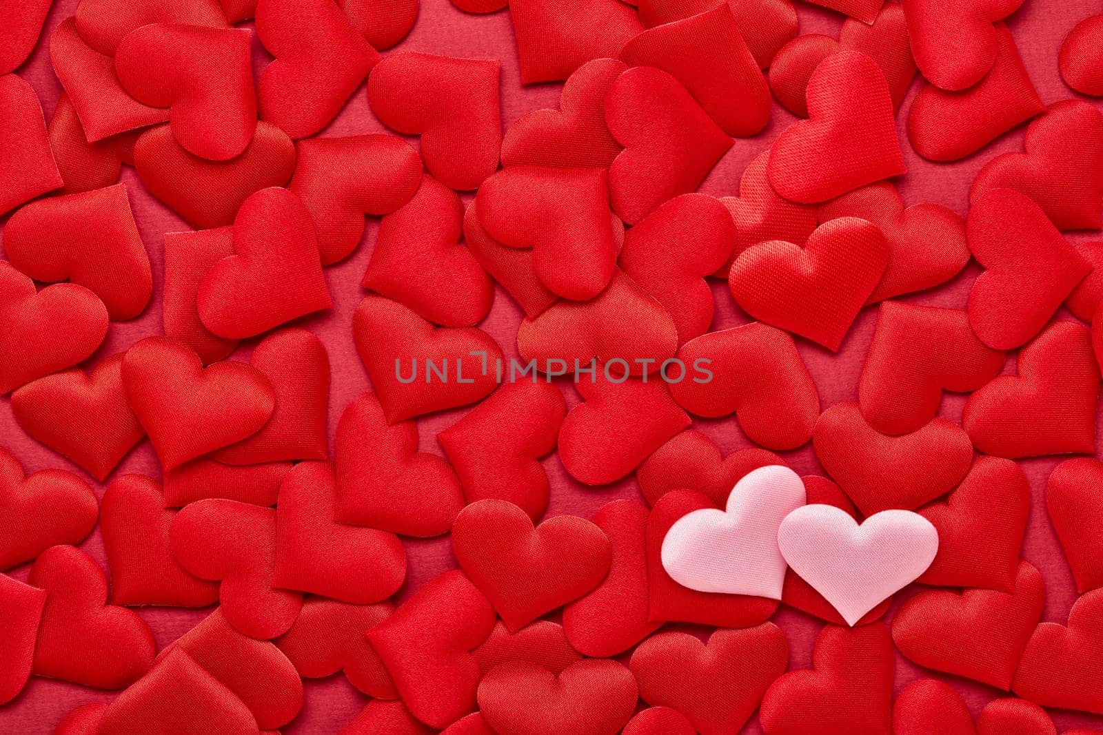 Two pink hearts on valentine background from red silk hearts. Valentine's Day. Top view with copy space. Design element for romantic greeting card, invitation. Hearts background. Wedding day
