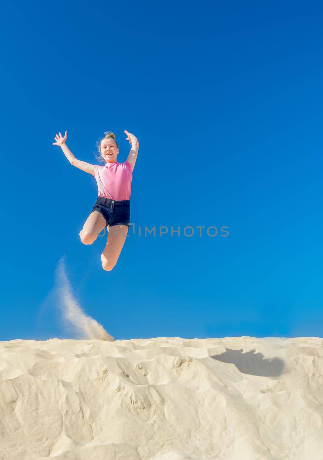 a young girl jumps in the summer from a yellow sand dune