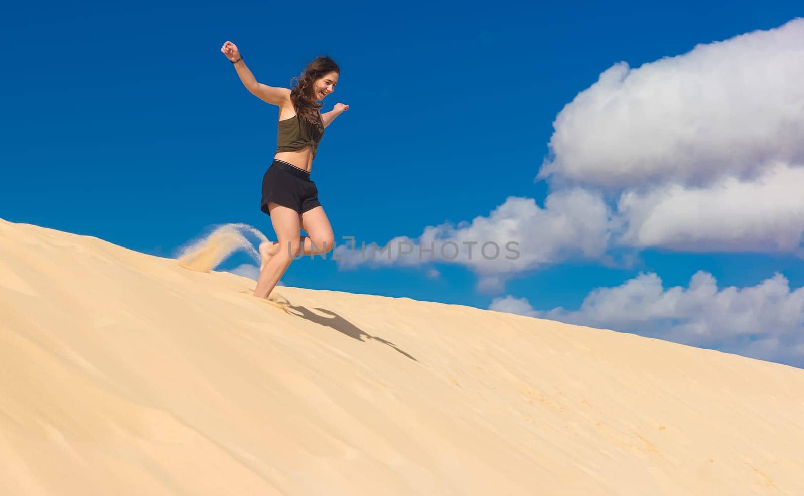 a girl runs from a sand dune full of zest for life in the summer, whirling up dust