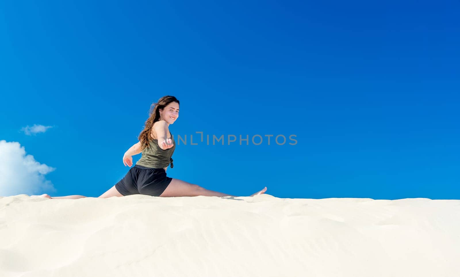 A young girl does yoga in the sand against a blue sky in summer