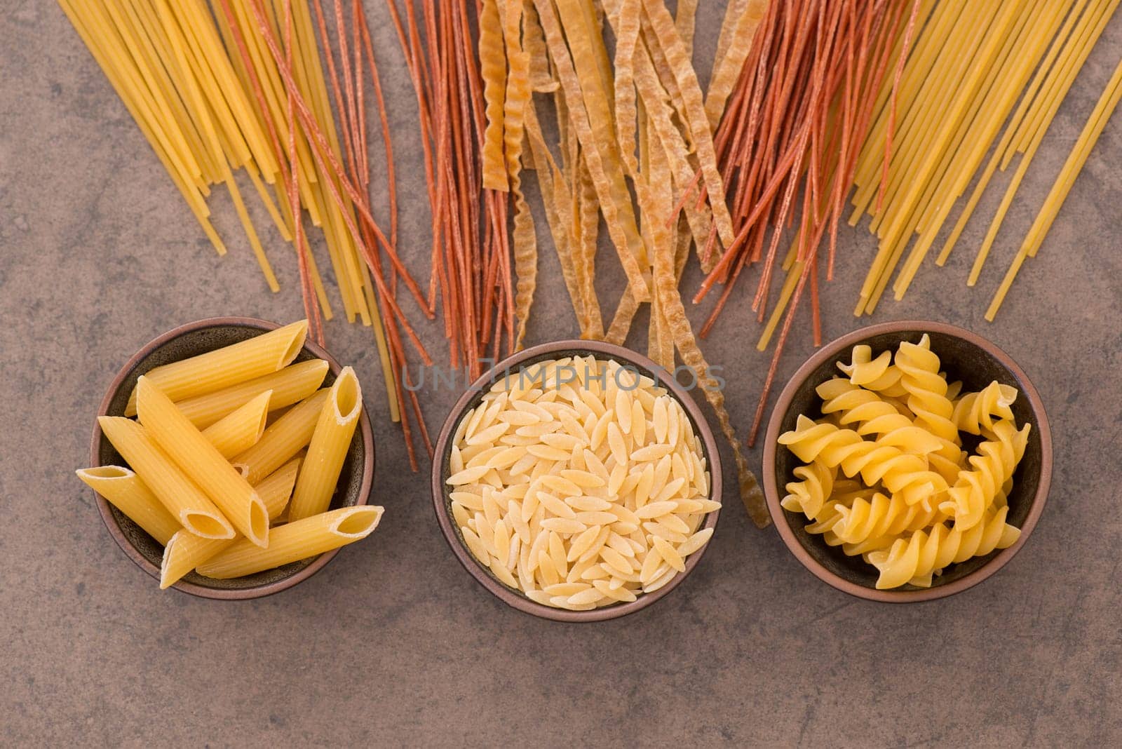 Mix of pasta made from wheat semolina, quinoa and azuki beans on a brown textured background, ingredients italian food