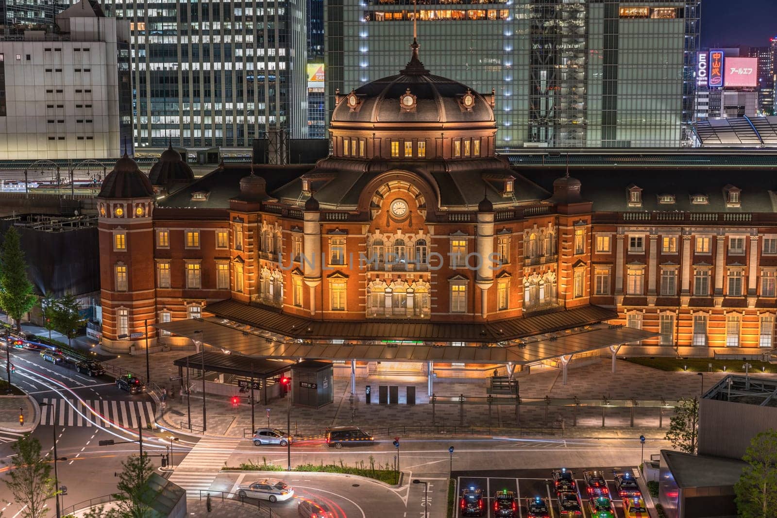 Night view of Marunouchi side of Tokyo railway station in the Chiyoda City, Tokyo, Japan.  The station is divided into Marunouchi and Yaesu sides in its directional signage. The station first called Central Station was built in 1914 directly in front of the Imperial Palace gardens. The three-story station building was designed by architect Tatsuno Kingo who also designed Manseibashi Station and the nearby Bank of Japan building. Much of the station was destroyed in B-29 firebombing on May 25, 1945. The bombing shattered the impressive rooftop domes. The station was quickly rebuilt within the year, but simple angular roofs were built in place of the domes, and the restored building was only two stories tall instead of three.