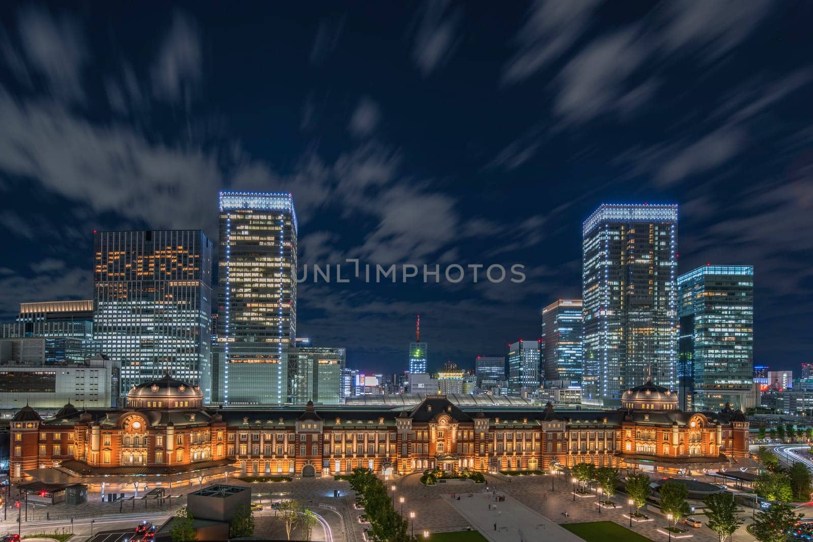 Night panoramic view of Marunouchi side of Tokyo railway station in the Chiyoda City, Tokyo, Japan.  The station is divided into Marunouchi and Yaesu sides in its directional signage. The station first called Central Station was built in 1914 directly in front of the Imperial Palace gardens. The three-story station building was designed by architect Tatsuno Kingo who also designed Manseibashi Station and the nearby Bank of Japan building. Much of the station was destroyed in B-29 firebombing on May 25, 1945. The bombing shattered the impressive rooftop domes. The station was quickly rebuilt within the year, but simple angular roofs were built in place of the domes, and the restored building was only two stories tall instead of three.