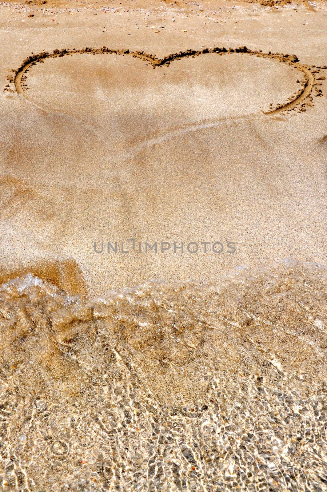 Hand drawn picture of the heart on wet beach sand.