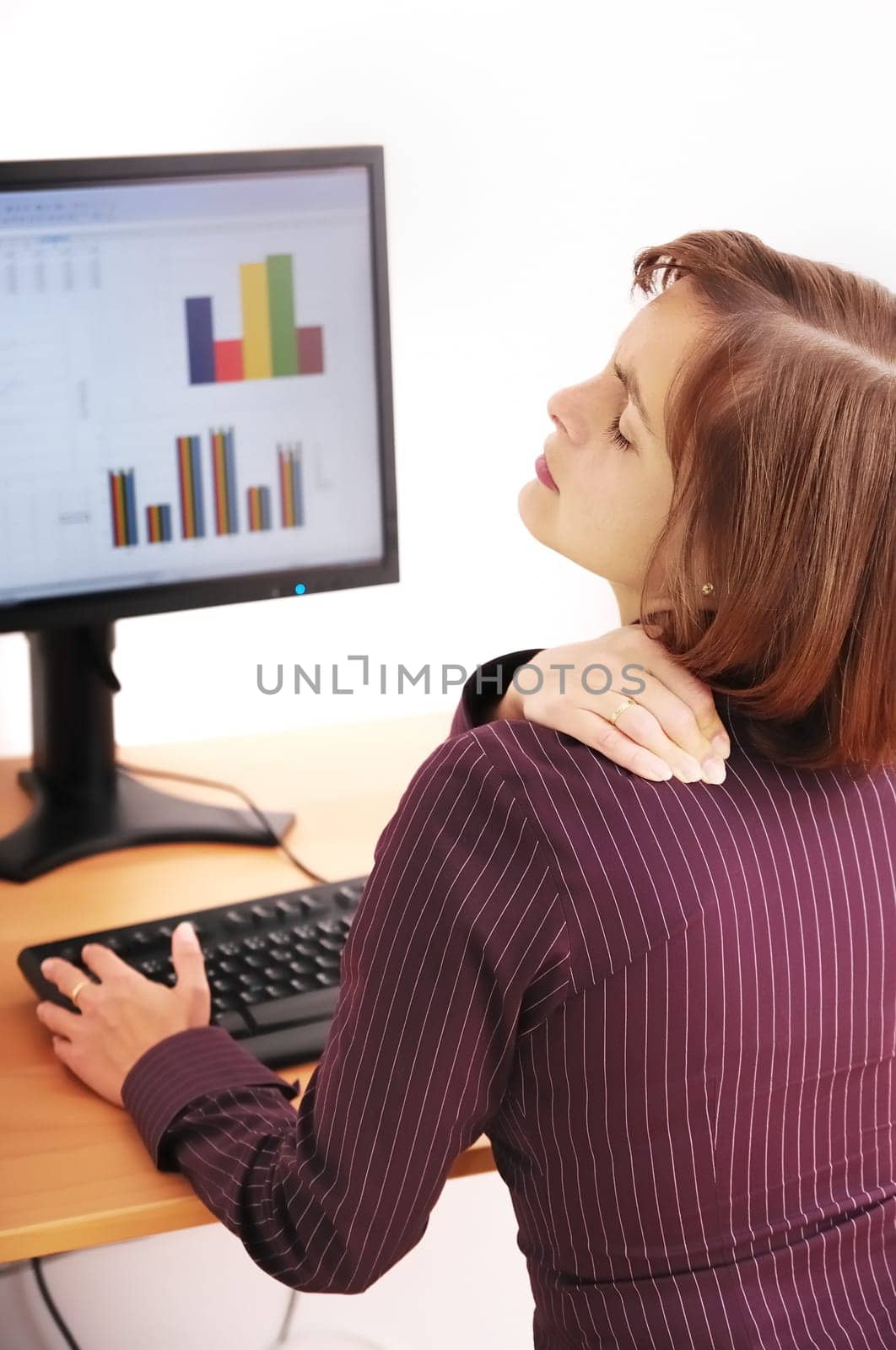 Business person with neck pain. Focus on hand on neck with blurred monitor on table in background.