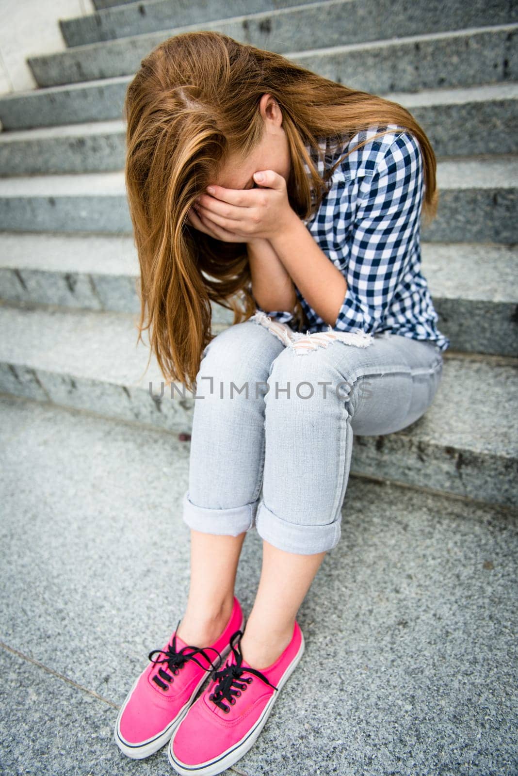 Unhappy depressed teenager with face in hands sitting outdoor
