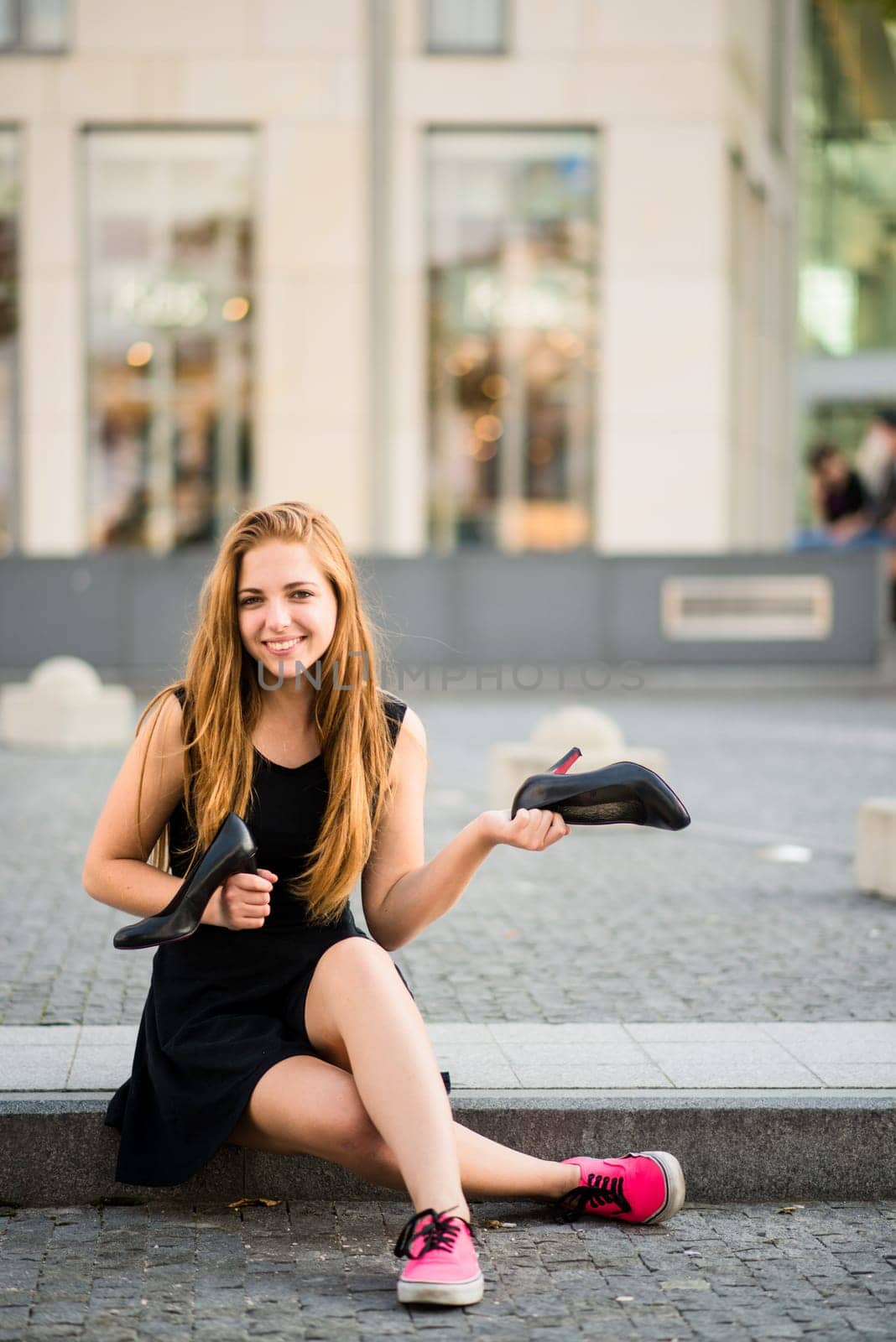 Teenager lifestyle - young woman on street in sneakers holding high heels shoes