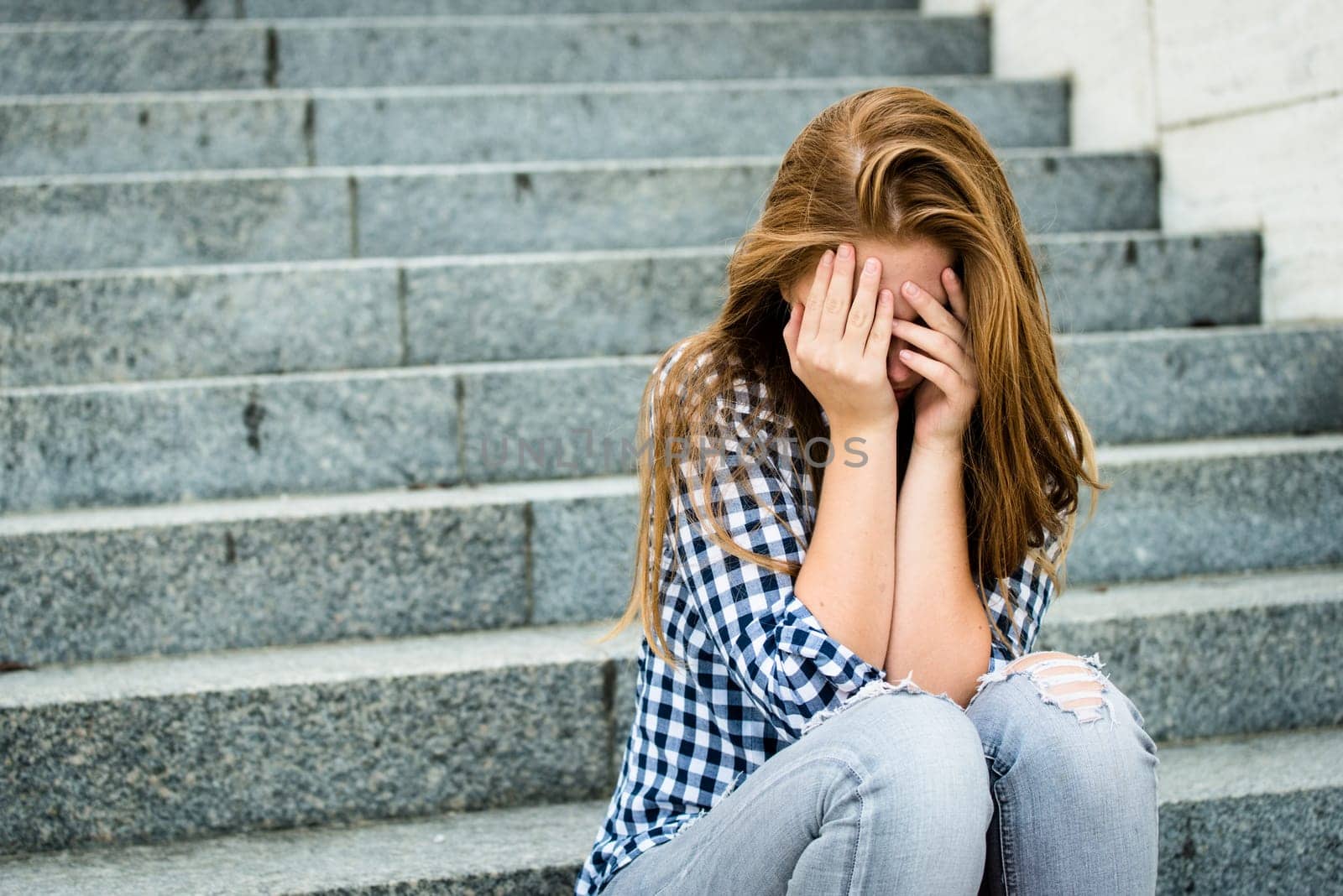 Unhappy depressed teenager with face in hands sitting outdoor