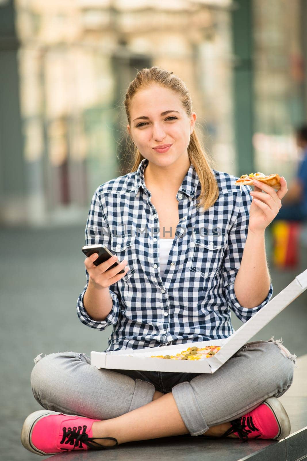 Teenager eating muffin in street and browsing internet on phone