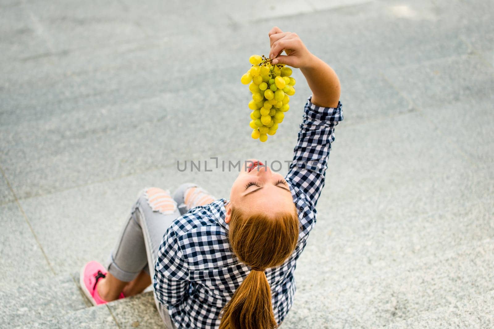 Young woman eating grapes outdoor sitting on stairs - above view