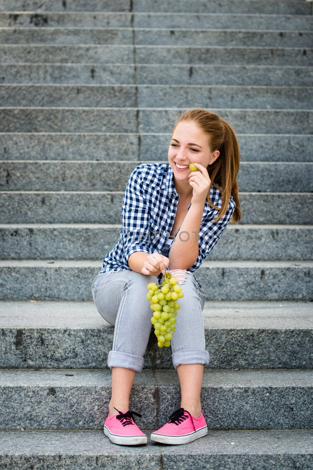 Young woman - teenage girl eating grapes outdoor sitting on stairs