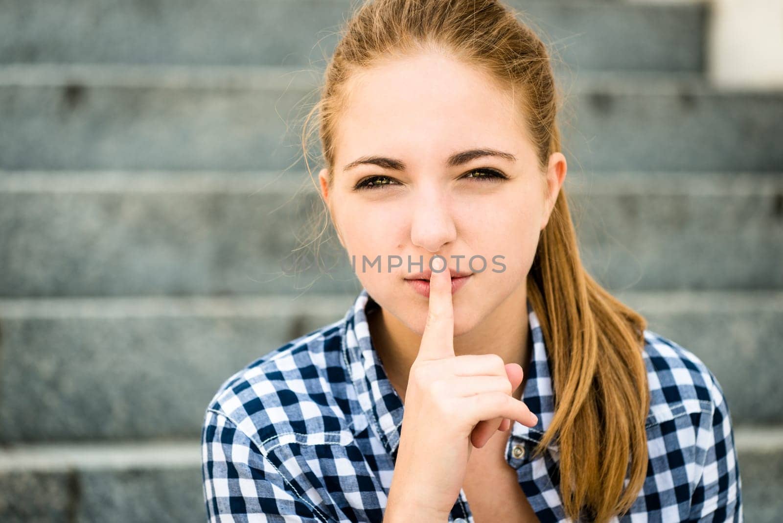 Teenager with finger on mouth as a sign of silence outdoor in street