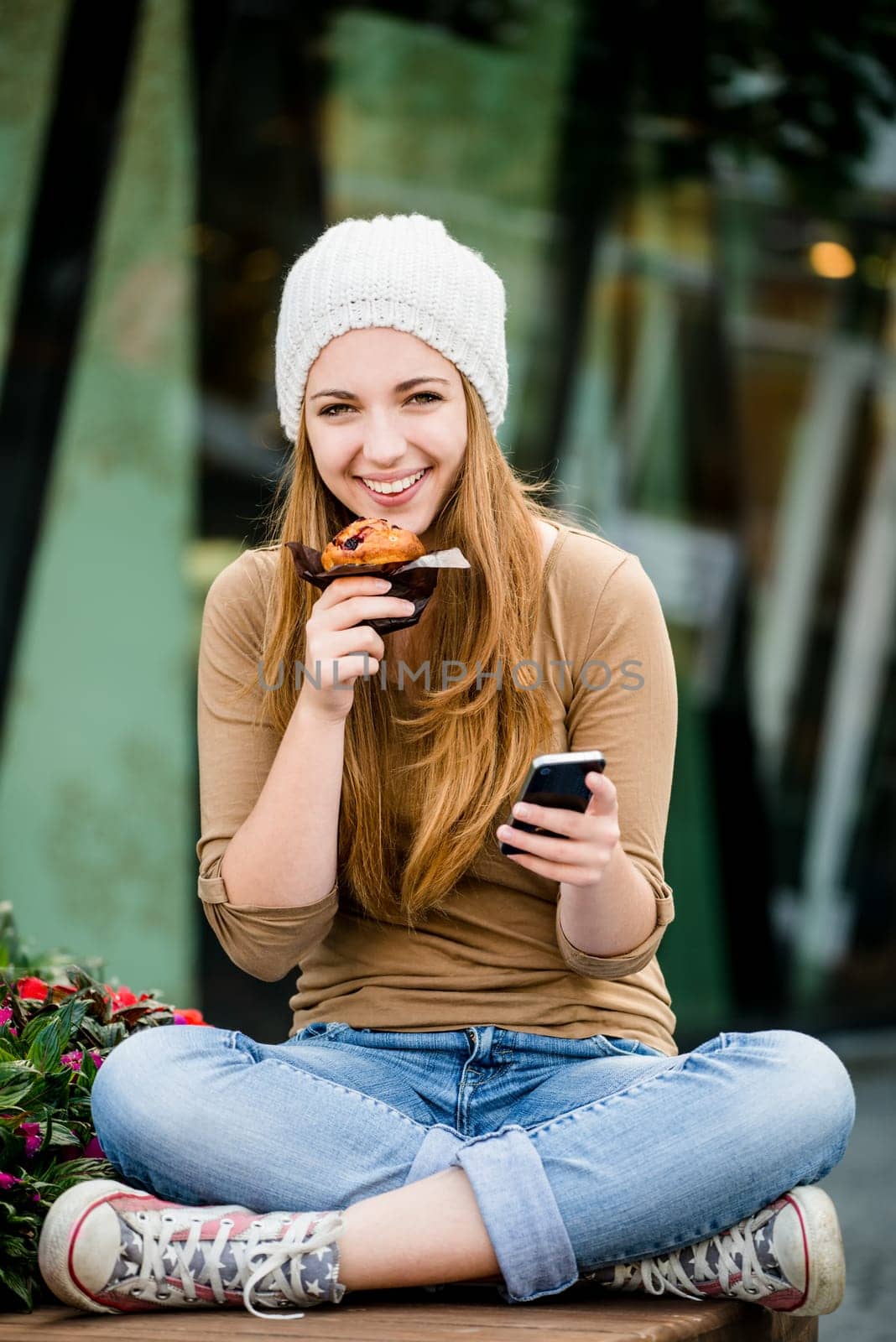Teenager - young woman eating muffin in street and looking in phone
