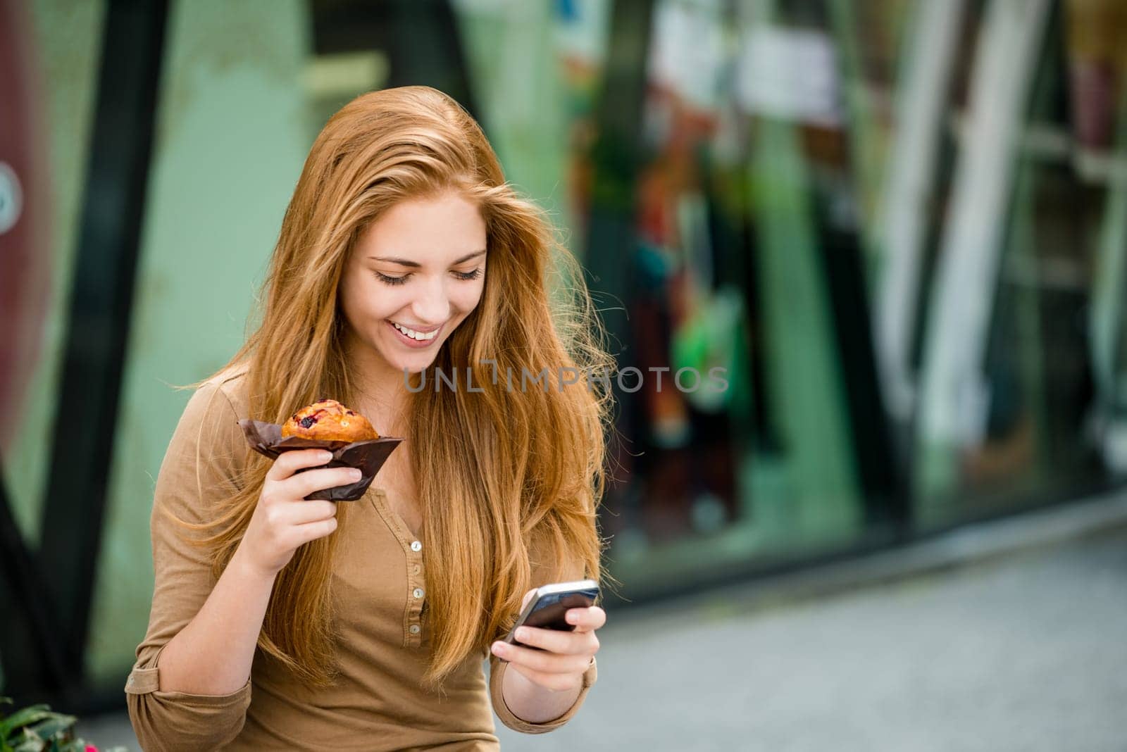 Teenager - young woman eating muffin in street and looking in phone