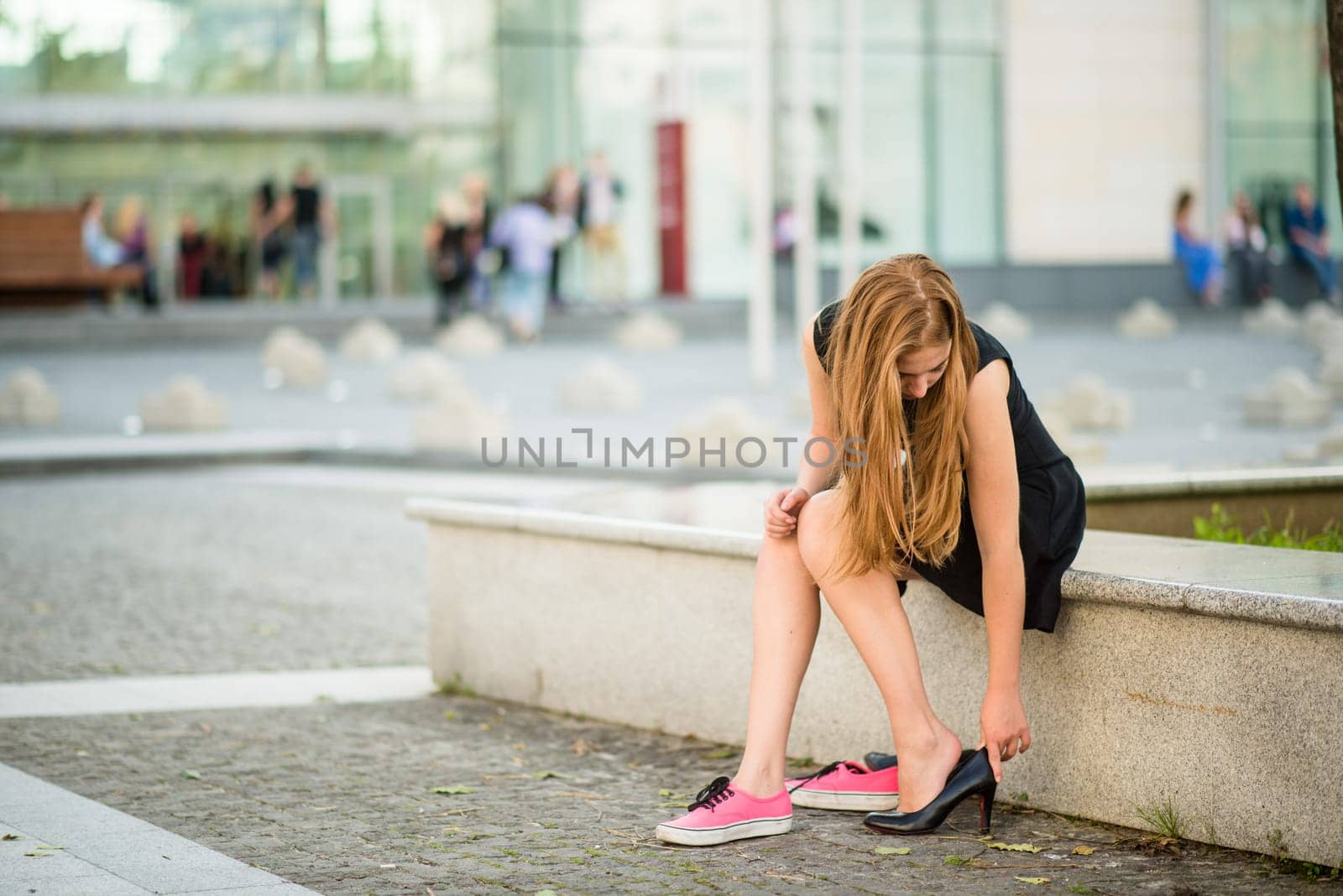Young woman changes shoes on street high heels instead of sneakers