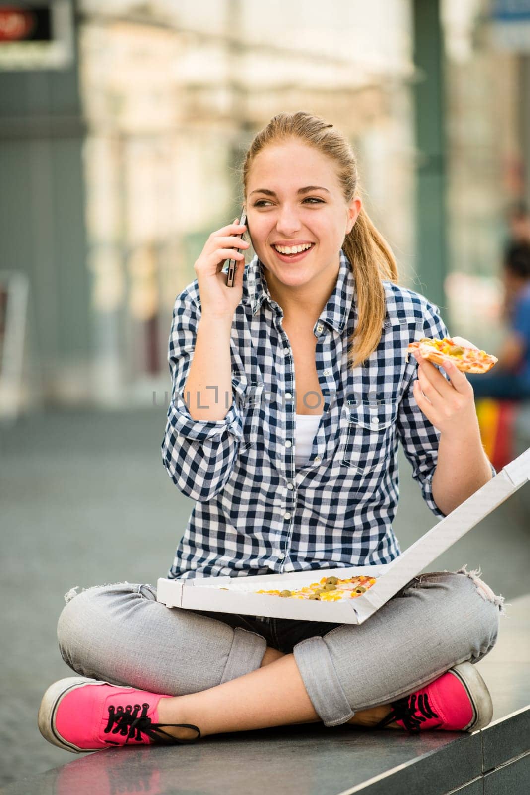 Young woman - teenage girl eating pizza in street and calling phone