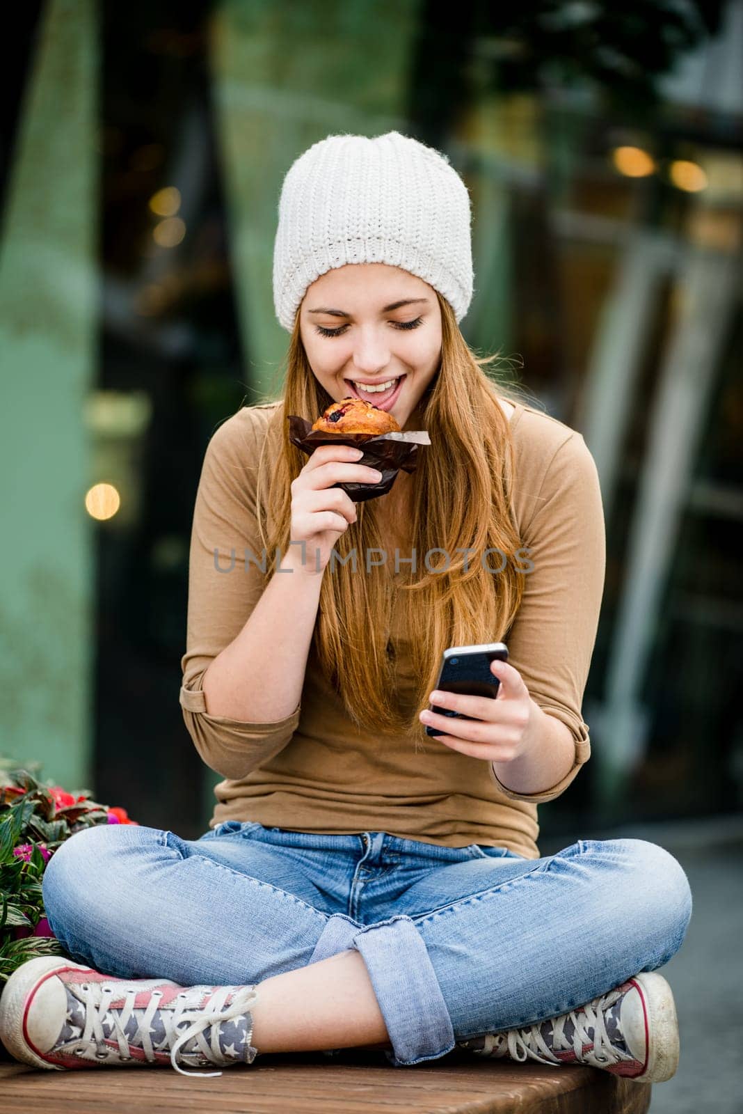 Teenager - young woman eating muffin in street and looking in phone