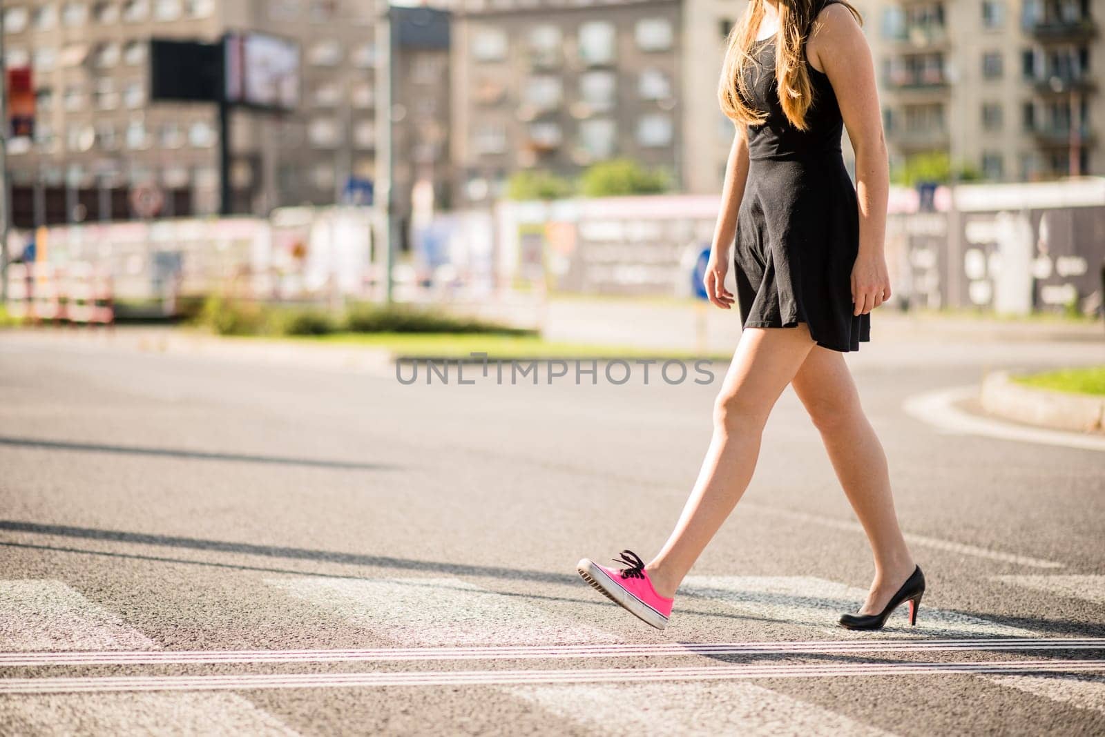 Young woman walking street - one foot in sneaker and other in high heel shoe