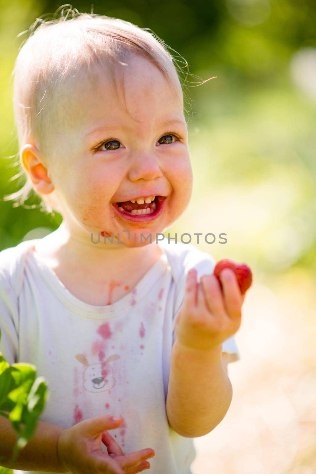 Pure joy - cute happy baby with strawberry, outdoor in garden