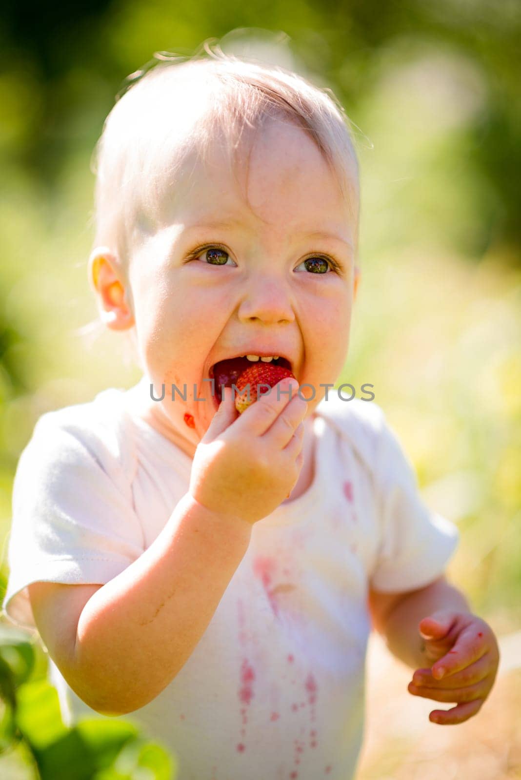 Happiness - cute baby eating strawberries, outdoor in garden