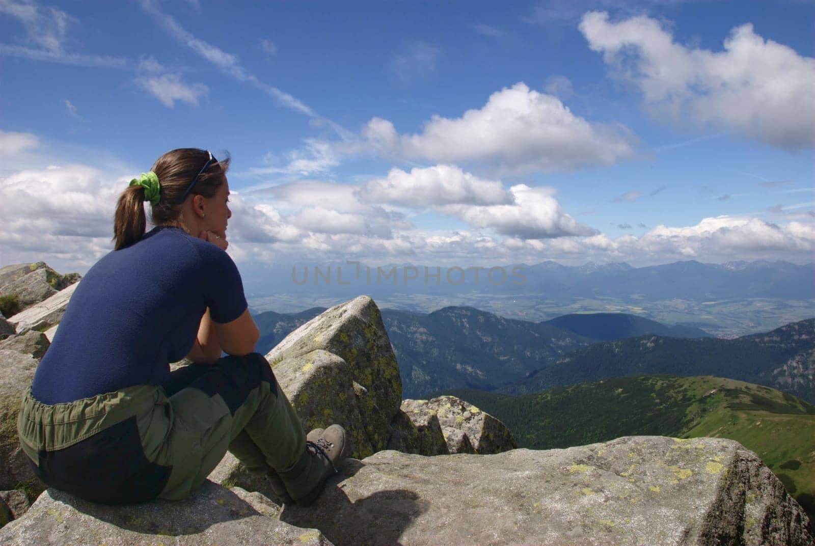 Hiking woman siting on rocks looks at beautiful  mountains and blue sky