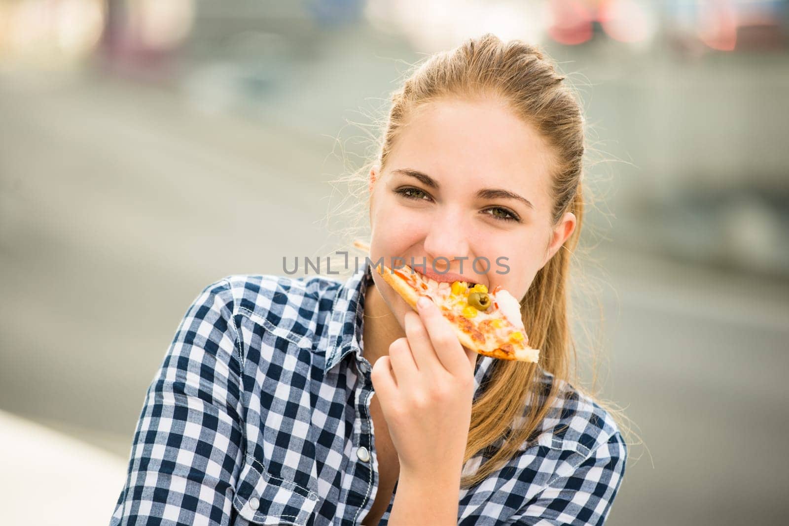 Teenager lifestyle - young woman eating pizza outdoor in street