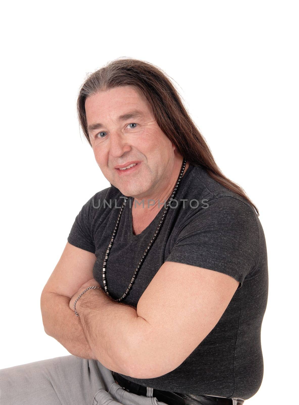 A happy indigenous man sitting for a portrait image on a chair with.his long brunette hair and arms crossed, isolated for white background.