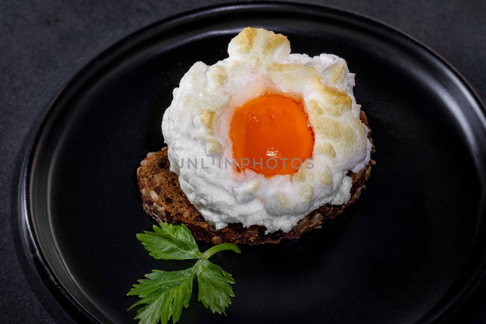 Delicate baked egg Orsini (eggs in the cloud). French breakfaston a piece of bread in a black ceramic dish