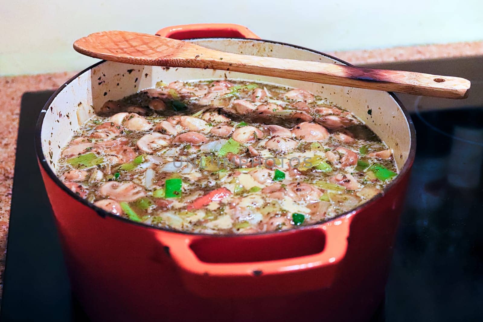 A pot of vegetables cooking with a wooden spoon on the edge.